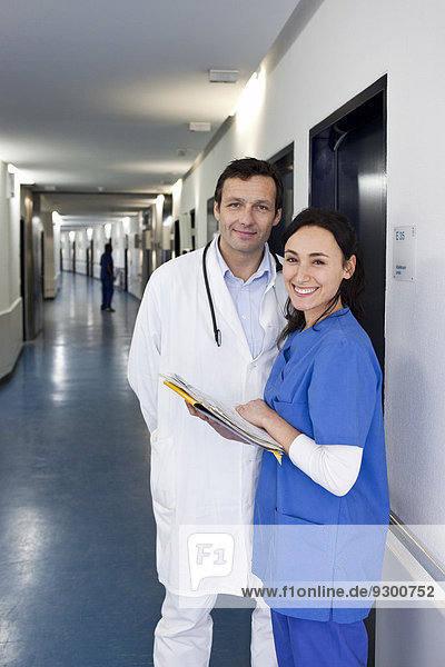 A nurse in scrubs consulting a doctor in a lab coat about a medical file  looking at camera