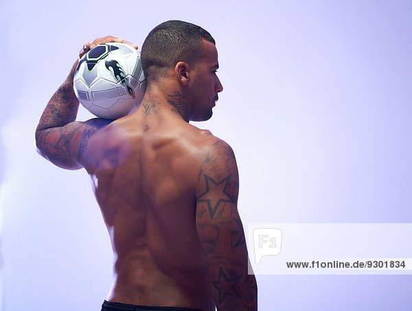 Studioaufnahme eines jungen männlichen Fußballspielers  der den Ball auf der Schulter hält.