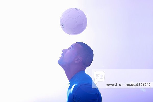 Studioaufnahme eines jungen männlichen Fußballspielers  der den Ball in der Luft hält  mit Kopfball
