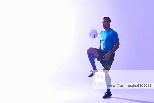 Studioaufnahme eines jungen männlichen Fußballspielers  der den Ball mit dem Knie in der Luft hält.