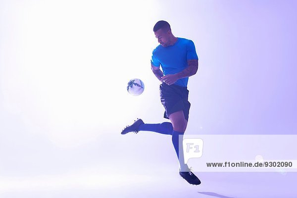 Studioaufnahme eines jungen männlichen Fußballspielers  der mit Rückstoß den Ball in der Luft hält.