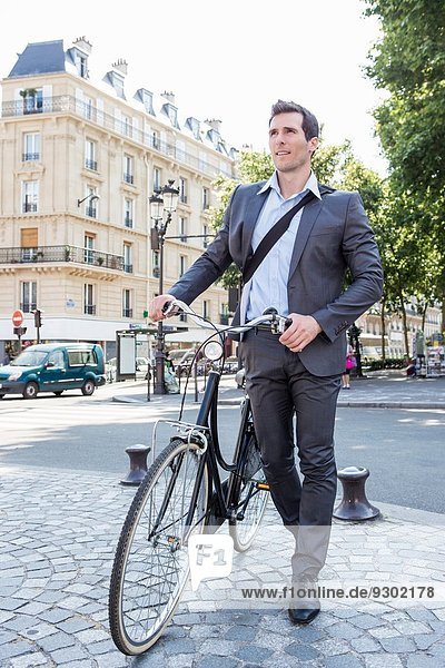 Mittlerer Erwachsener Geschäftsmann  der Fahrrad über Kopfsteinpflaster schiebt  Paris  Frankreich