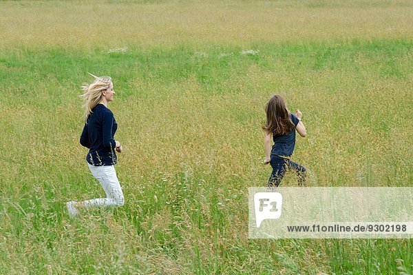 Mutter und Tochter rennen durch langes Grasfeld