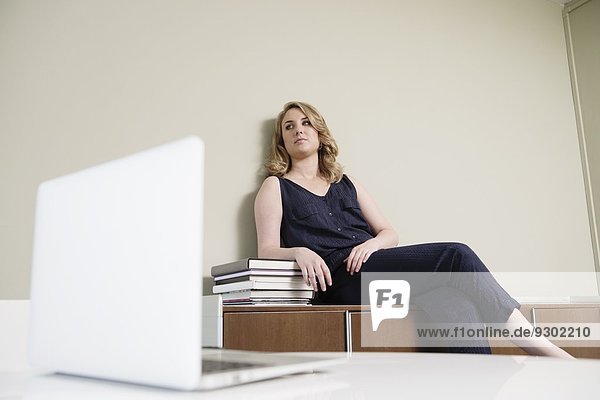 Junge Geschäftsfrau sitzt auf Schrank in neuem Büro