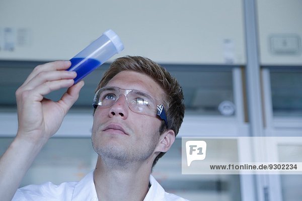 Männlicher Wissenschaftler betrachtet Probe in Plastikflasche im Labor