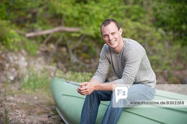 Portrait eines jungen Mannes  der auf einem umgedrehten Boot sitzt.
