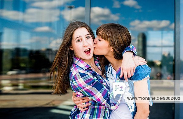 Two young women fooling around hugging with kiss on cheek