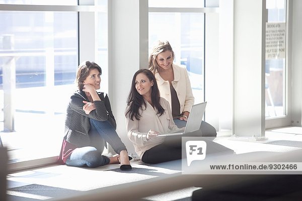Three businesswomen sitting on floor with laptop in conference centre