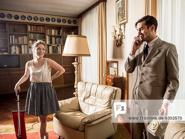 Young vintage couple in sitting room with vintage telephone and vacuum cleaner