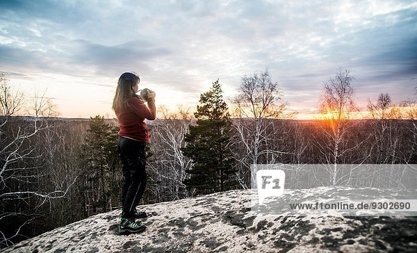 Young woman on top of rock photographing sunset