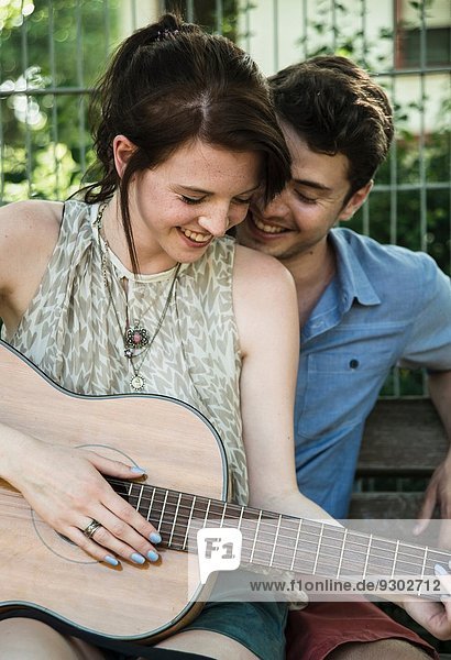 Junges Paar singt auf Akustikgitarre im Park