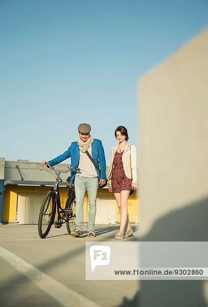 Young couple pushing bicycle along street