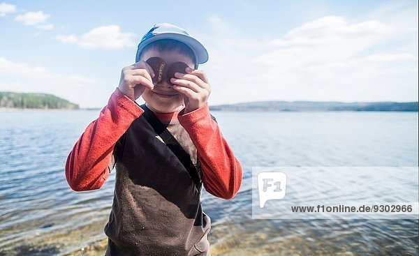 Porträt des schelmischen Jungen mit Keksen über den Augen am Seeufer