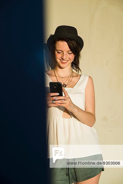 Junge Frau lehnt sich an die Wand und liest Text auf dem Smartphone.