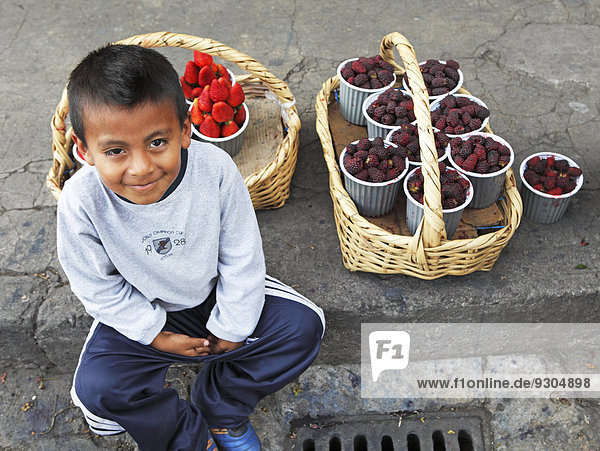 Boy with fruit punnets sitting on the curb of a street  Ibarra grocery market  Imbabura Province  Ecuador