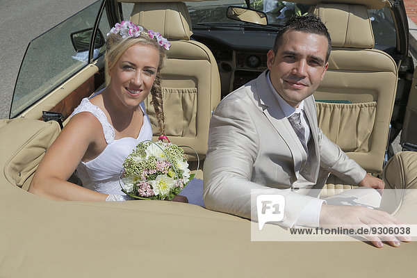 Bride and groom posing in the back seat of an open car  convertible