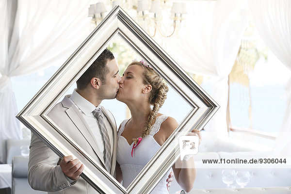 Bride and groom holding a picture frame in front of them  kissing  photo shoot