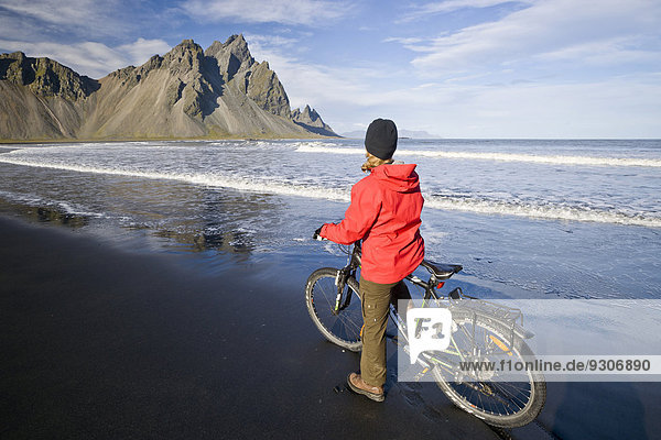 Woman riding a bicycle on the beach in front of Mt Vestrahorn near Hoefn  Stokksnes  Southwest Iceland  Iceland