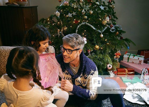 Father and two daughters opening christmas gifts in sitting room