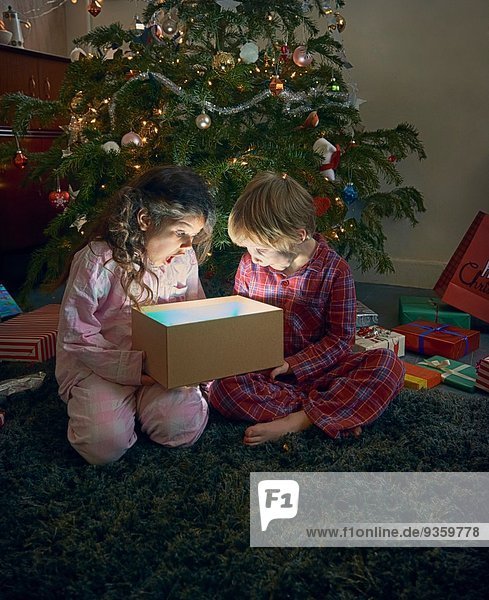 Schwester und Bruder öffnen den Mund und packen die glühende Weihnachtsgeschenkbox aus.