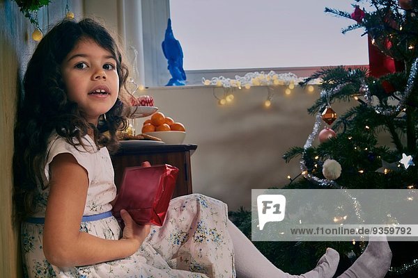 Porträt eines auf dem Boden sitzenden Mädchens mit Weihnachtsgeschenk