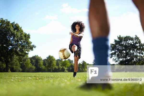 Young woman kicking soccer ball toward boyfriend in park