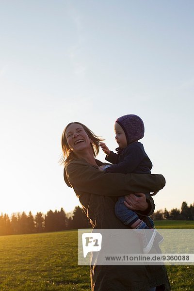 Reife Mutter und kleine Tochter lachend im Feld bei Sonnenuntergang