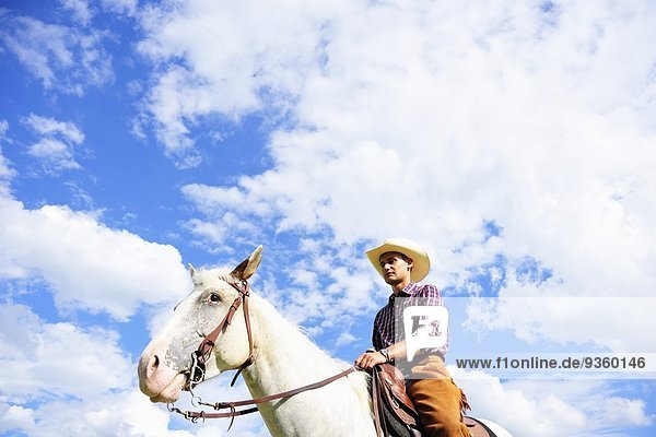 Niederwinkel-Porträt eines jungen Mannes in Cowboy-Ausrüstung Reitpferd