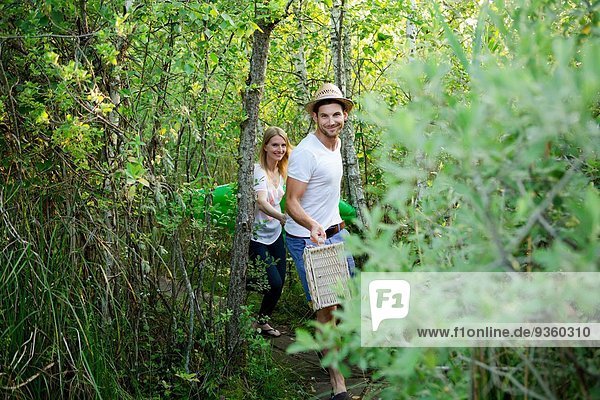 Mid adult couple walking through marshland with picnic basket