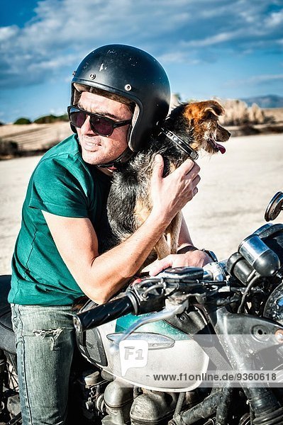 Mittlerer Erwachsener Mann und Hund sitzend auf Motorrad auf trockener Ebene,  Cagliari,  Sardinien,  Italien