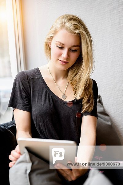 Junge Frau mit digitalem Tablett im Fenstersitz