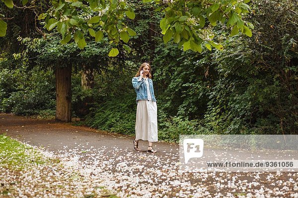 Junge Frau plaudert auf dem Smartphone beim Spaziergang im Park