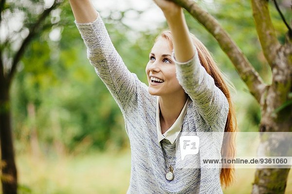 Junge Frau im Feld  die sich an einem Baumzweig festhält