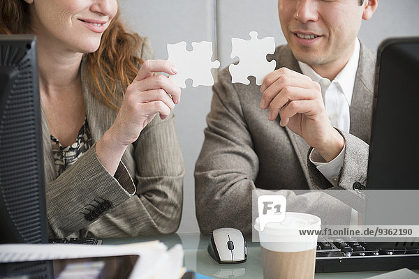 Business people putting puzzle pieces together at desk
