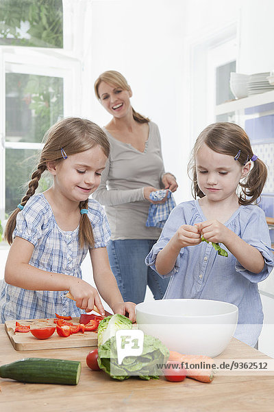 Deutschland  München  Mädchen (4-7) hacken Gemüse in der Küche  Mutter steht im Hintergrund