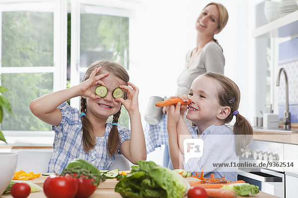 Deutschland  München  Mädchen (4-7) spielen mit Gemüse in der Küche  Mutter steht im Hintergrund
