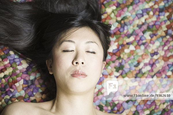 Porträt einer Asiatin mit geschlossenen Augen vor farbigem Grund