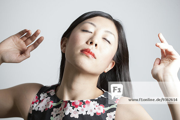 Porträt einer Asiatin mit geschlossenen Augen vor grauem Hintergrund