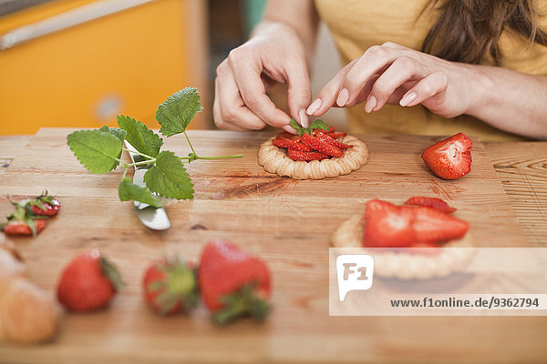 Junge Frau garniert Kuchen mit Erdbeeren und Minze  Teilansicht