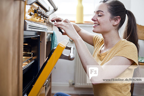 Porträt einer lächelnden jungen Frau beim Fotografieren von Gebäck in ihrem Ofen