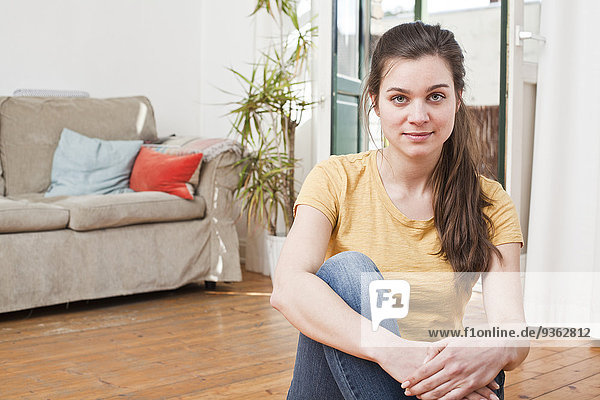 Porträt einer jungen Frau  die auf dem Boden ihres Wohnzimmers sitzt.
