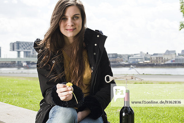 Germany    portrait of smiling young woman with red wine bottle sitting in front of Rhine River