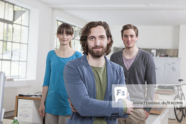 Porträt eines jungen Mannes mit seinen beiden Kollegen im Hintergrund in einem Kreativbüro