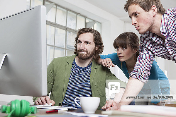 Drei Kollegen beim Blick auf den Computer in einem Kreativbüro