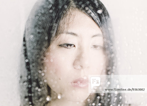 Young woman looking through a window with water drops