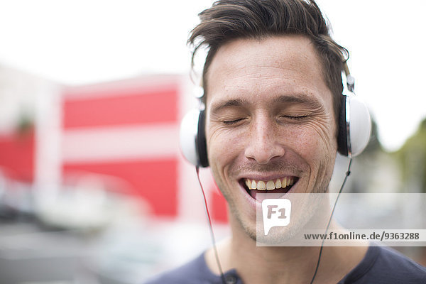 Portrait eines singenden jungen Mannes  der mit Kopfhörern Musik hört.