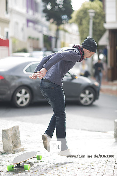 Junger Mann springt von seinem Skateboard auf einem Bürgersteig