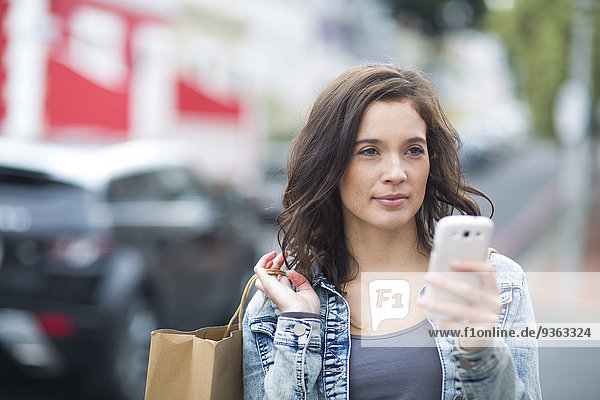 Porträt einer Frau mit Einkaufstasche und Smartphone  die auf der Straße geht