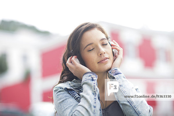 Portrait einer jungen Frau mit geschlossenen Augen beim Musikhören mit Kopfhörern