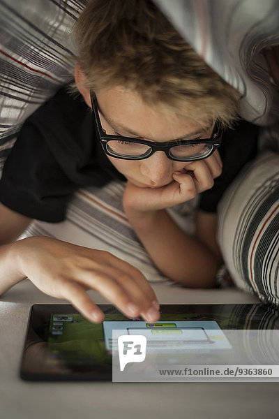 Junge auf dem Bett liegend mit digitalem Tablett